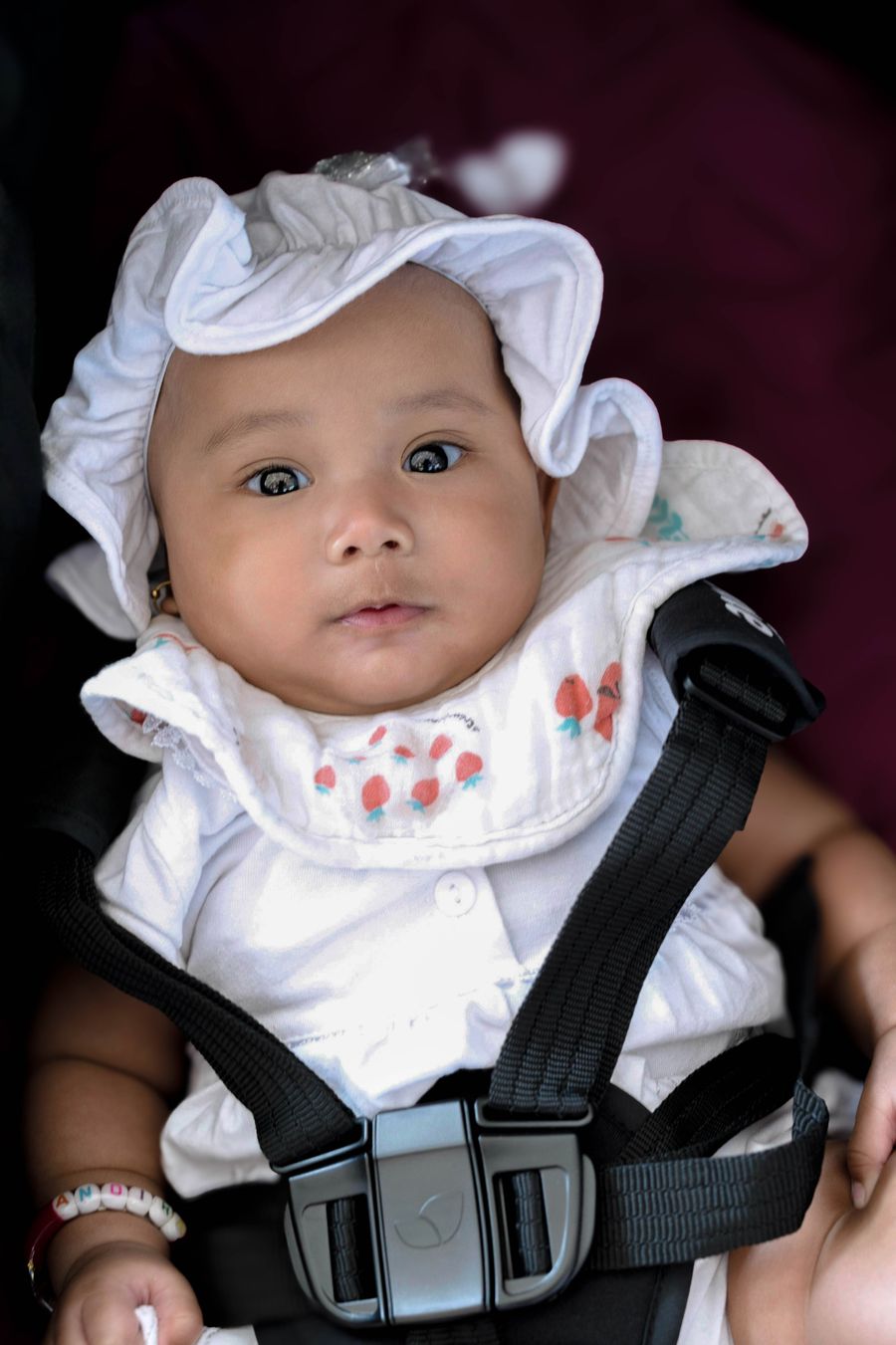 baby buckled safely into a car seat wearing a white hat before a family road trip