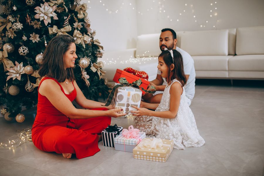 family exchanging baby's first Christmas gifts by a decorated Christmas tree on Christmas morning