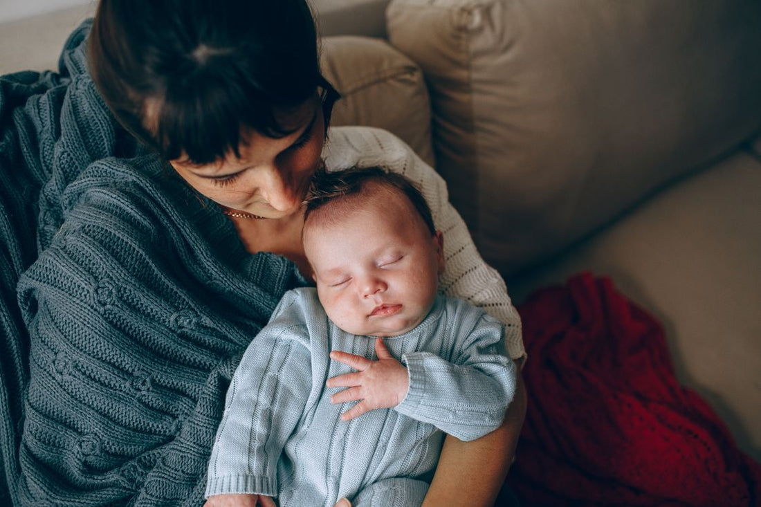 new mom resting on the couch with her sleeping newborn baby during a quiet December afternoon