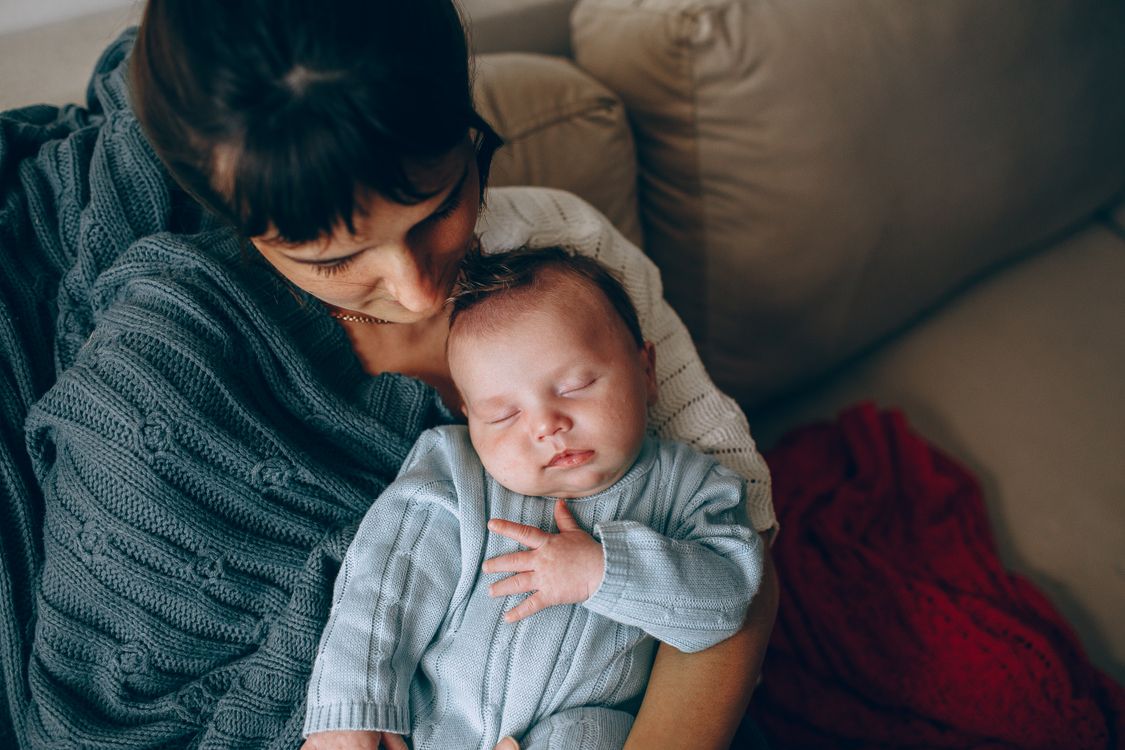 new mom resting on the couch with her sleeping newborn baby during a quiet December afternoon