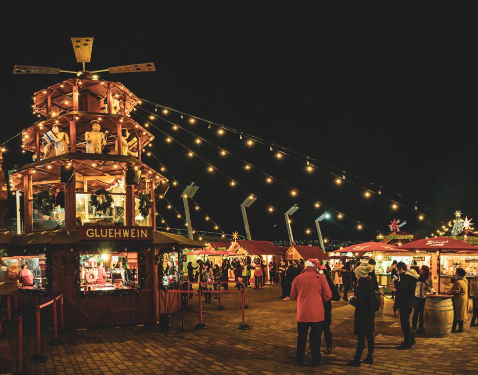 families strolling through a Christmas market with festive lights at night
