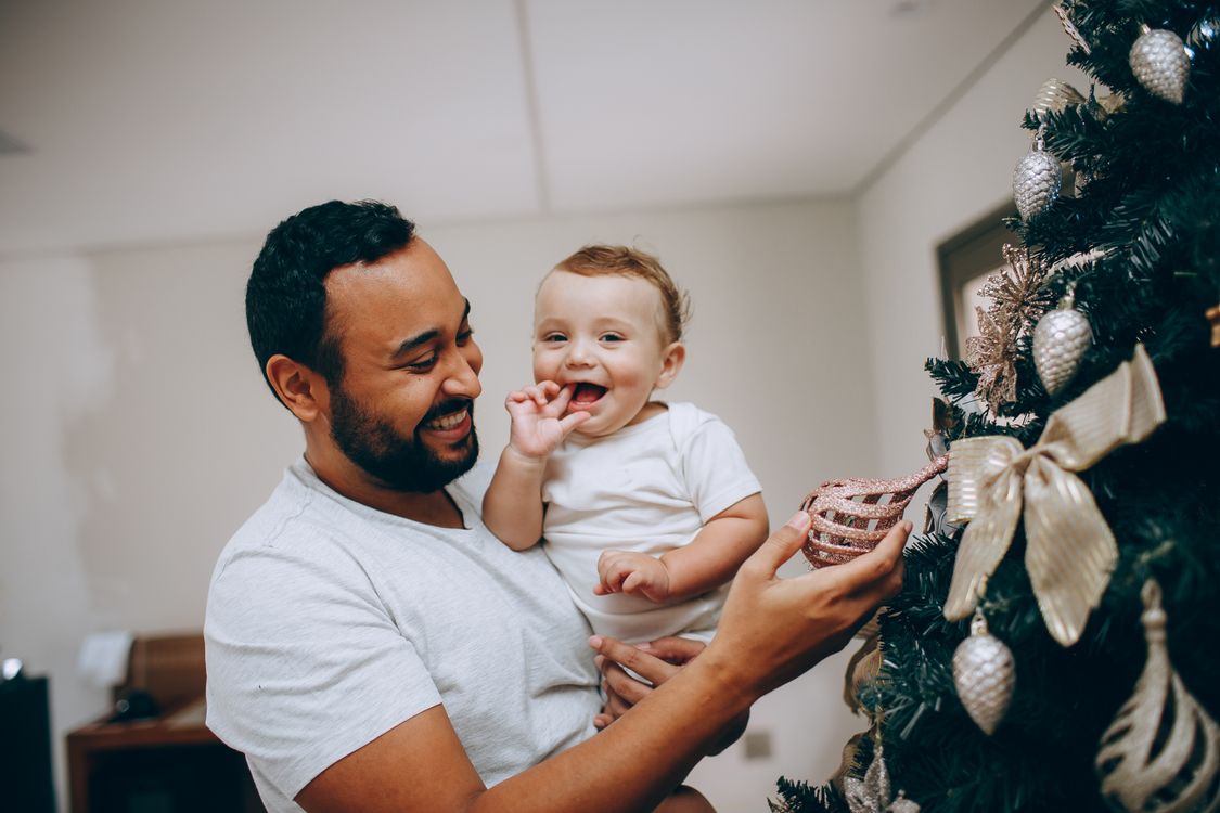 father holding a smiling baby in front of a decorated Christmas tree on Christmas Eve