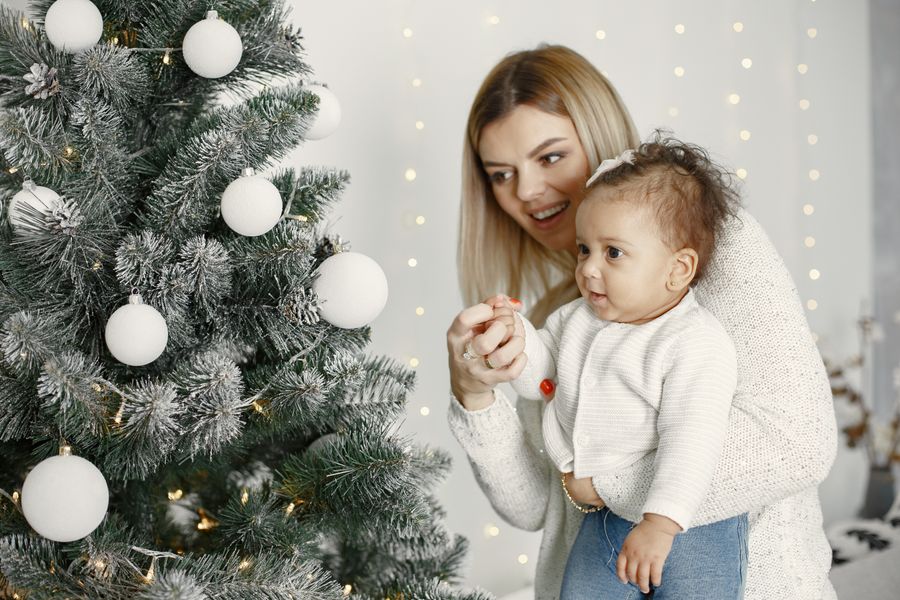 Mother showing her toddler the decorated Christmas tree on baby's first Christmas morning